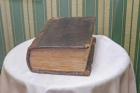 An old, worn book sits on a white-clothed table in an antiquated study room.. Stock Photos
