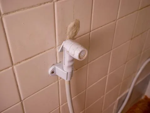 Old worn white plastic bidet hand sprayer mounted on beige ceramic bathroom.. Fotos Stock