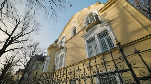 Old yellow building with grated windows and forged fence among bare trees Stock Footage 319891364