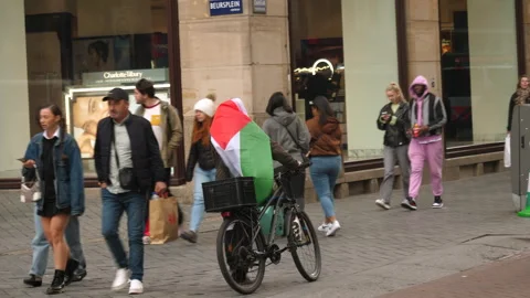 Older Arab man wrapped in Palestinian flag walks his bicycle in Amsterdam. Stock Footage 253263393
