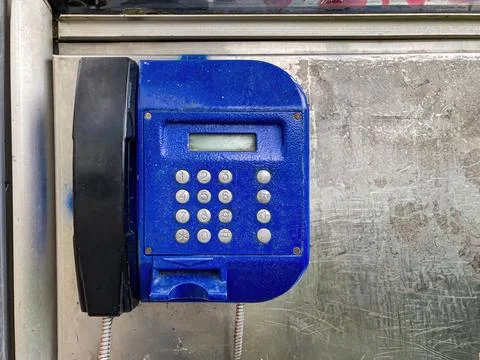 An older, blue push-button payphone leans slightly on a wall It has a blank.. Stock Photos
