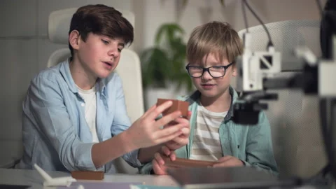 Older boy explains to a boy with glasses how a part was printed on a 3D printer Stock Footage 335376097