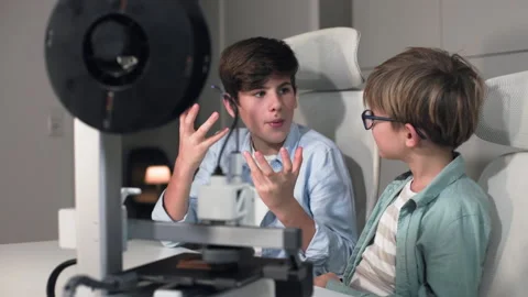 A older boy explains to his friend wearing glasses how a 3D printer works Stock Footage 335374695