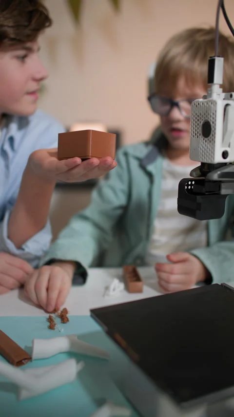 Older boy hold a 3D printed box in which boy in glasses place small 3D parts Stock Footage 335392976