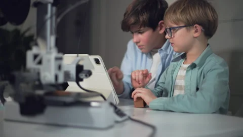 The older boy will not let the younger one operate the 3D printer by laptop Stock Footage 335377856