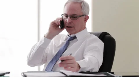 Older caucasian businessman at desk talking on cell phone Stock Footage