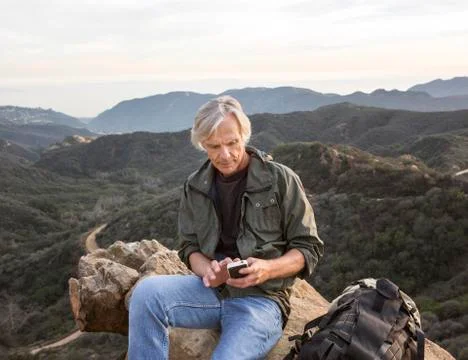 Older Caucasian man using cell phone on rocky hilltop 스톡 사진