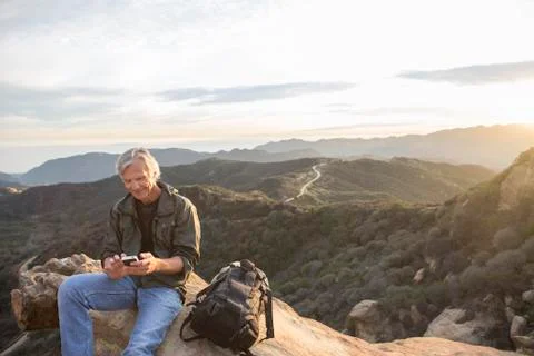 Older Caucasian man using cell phone on rocky hilltop 스톡 사진