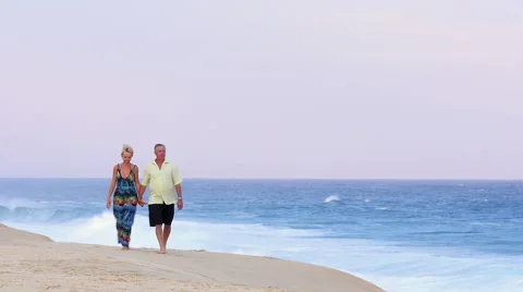 An older couple holding hands and walking down the beach Stock Footage