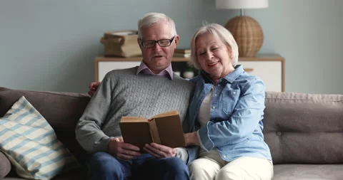 Older couple sitting on sofa discuss book plot Stock Footage 229621240
