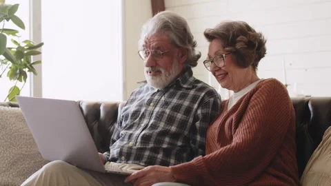 Older couple using computer laptop on sofa at home for online shopping Stock Footage 244117379