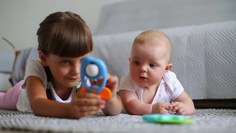 Older dark haired sister with two pigtails playing with little newborn girl. Stock Footage 157818974