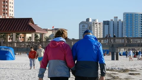 Older Elderly Couple Walking On White Sandy Beach On Cool Day With Hotel Res Stock Footage 127186488
