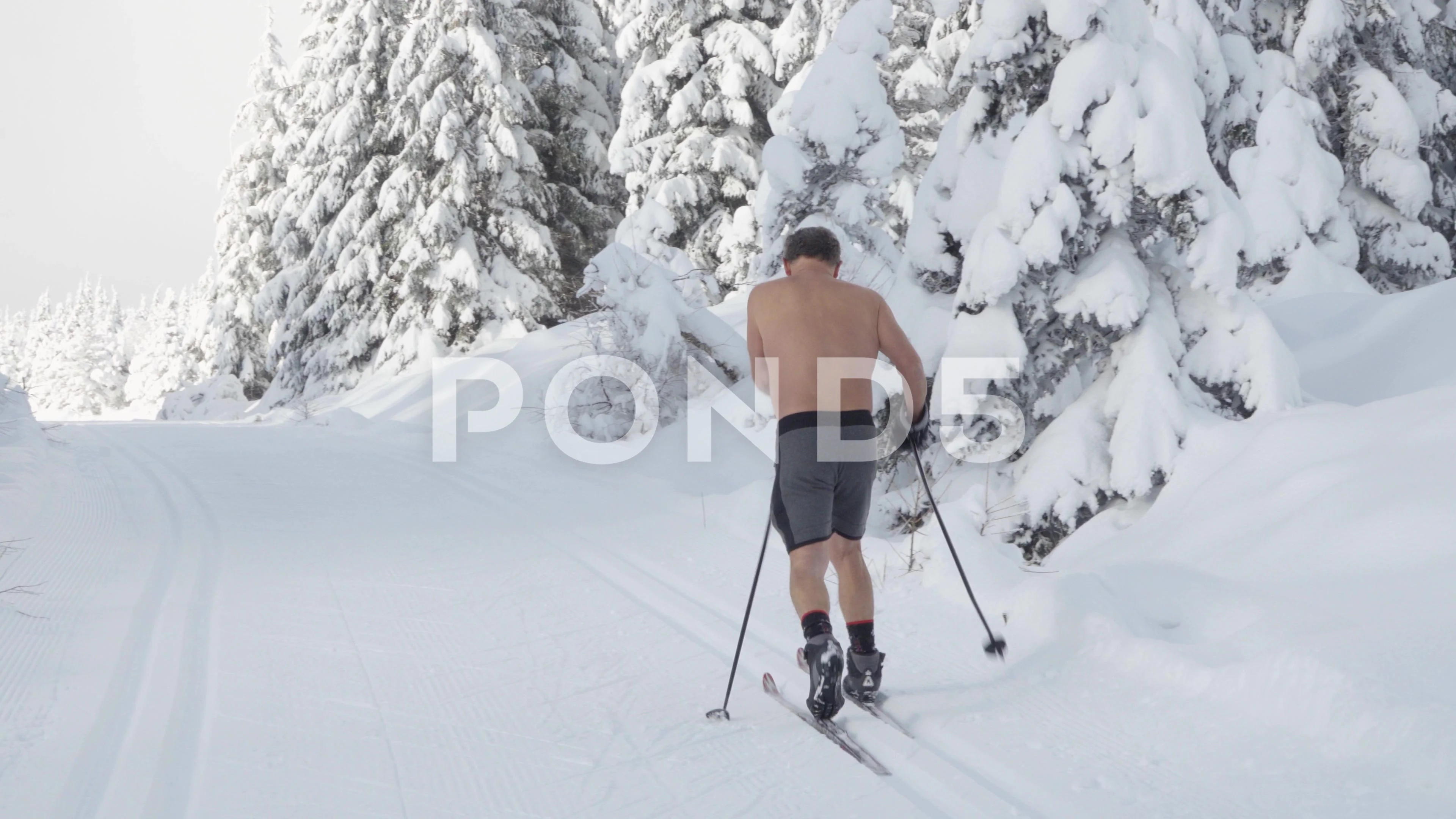 An older half-naked cross-country skier skies up a trail in a snow-covered