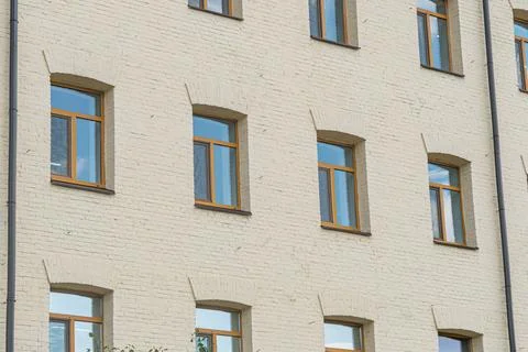 An older, light-brick building with evenly spaced windows framed in wood, dis Stock Photos