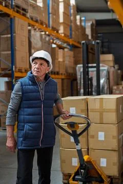 Older male warehouse worker pulling a pallet truck. Stock Photos