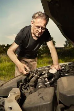 Older man alone on route checking unfunctional engine in late summer light Stock Photos