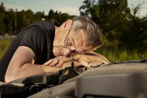 Older man alone on route checking unfunctional engine in late summer light Stock Photos