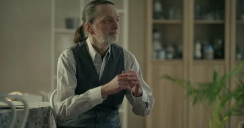Older man in apron standing in a softly lit kitchen 스톡 동영상 336276808