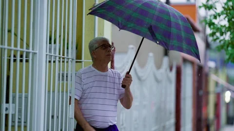 Older man arriving home while raining, opens gate and closes umbrella. Seni.. Stock Footage 252666155