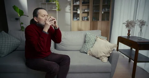 Older man calmly drinking from a glass while sitting on a sofa at home Stock Footage 336288860