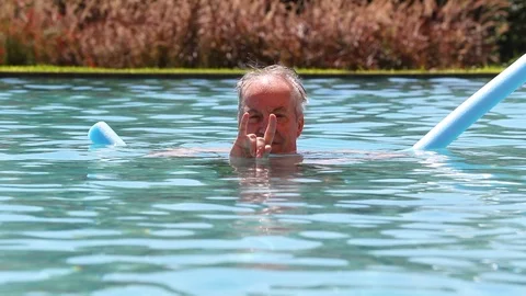Older man doing devil sign with hands while at the swimming pool looking to c Stock Footage 116799836