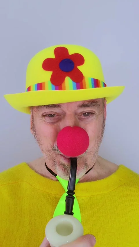 Older man dressed as a clown performs a magic trick with a pipe that turns into Stock Footage 330802747