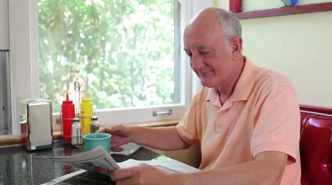 Older man drinking coffee and reading paper in a diner Stock Footage 7825636