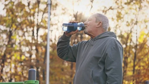 An older man is drinking water from a bottle in a park Stock Footage 264323665