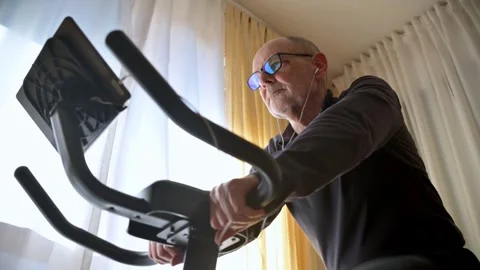 Older man focused on a home workout using a stationary exercise bike Stock Footage 336044160