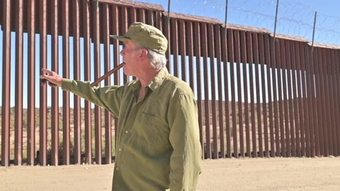 Older man in front of border wall dividing United States and Mexico, Stock Footage 168721440