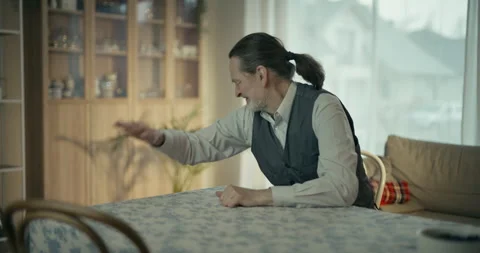 Older man gesturing while talking in a bright home living room workspace 스톡 동영상 336276314