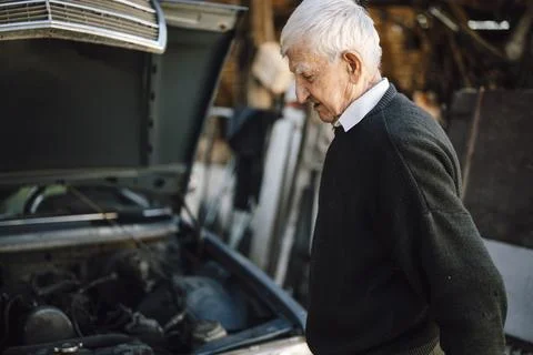 Older man inspecting car engine in rural workshop Stock Photos