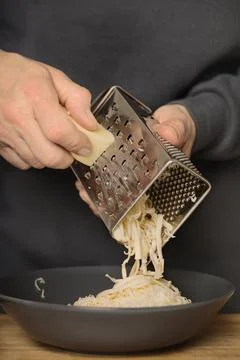 Older man in kitchen grating cheese for spaghetti with minced meat, tomatoes  Stock Photos
