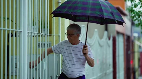 Older man leaving home while raining, opens umbrella and closes gate behind.. Stock Footage 252677498