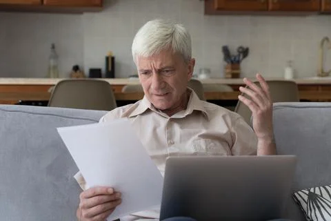 Older man looks dissatisfied while read unpleasant notification from bank Stock Photos