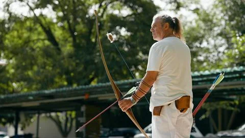Older man practicing archery, aiming for goals outdoors Stock Photos