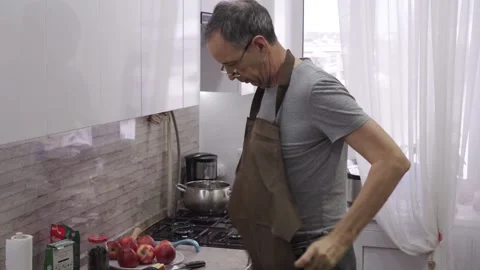 An older man puts on an apron while standing in the kitchen Stock Footage 168521226