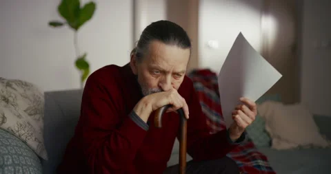 Older man reading a document while sitting on a sofa in a cozy living room Stock Footage 336279463