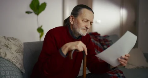 Older man reading papers on a sofa in a softly lit living room Vídeos de archivo 336278229