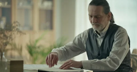 Older man reading papers at a table in a calm sunlit indoor room Stock Footage 336287620