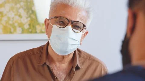 An older man recieves a parcel delivery from a courier wearing a mask. Working Stock Photos