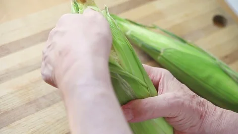 Older man removes husk from corn Stock Footage 76087944