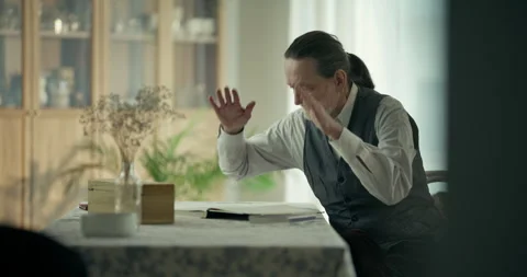 Older man reviewing papers at a dining table in a softly lit home interior Stock Footage 336278577