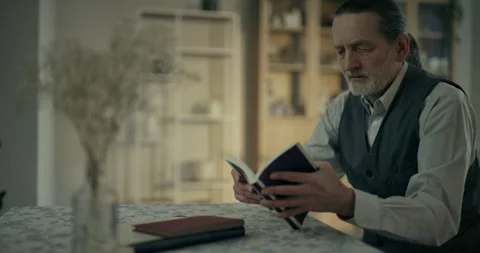 Older man reviewing papers at a table in a quiet home interior Stock Footage 336289025
