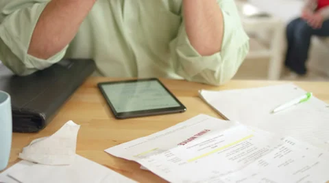 An older man sits at the table looking at a large stack of unpaid bills Stock Footage 34012505
