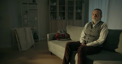 Older man sitting alone on a sofa in a dim living room Stock Footage 336288234