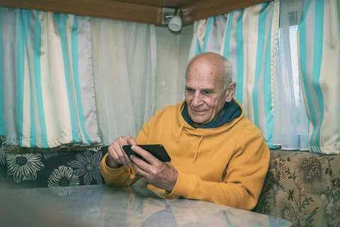 Older man sitting at desk using and checking smartphone in camping rv 스톡 사진
