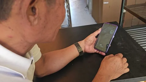 Older Man Sitting At Table Swiping Smartphone Screen Watching Short Videos Stock Footage 340013619