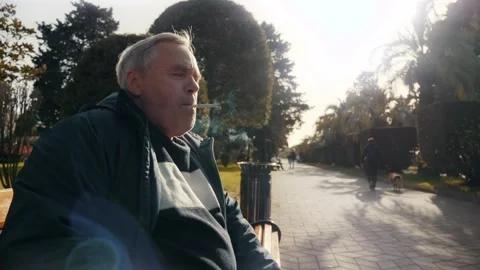 Older man smoking cigarette in public place, highlighting health risks Stock Footage 303523640